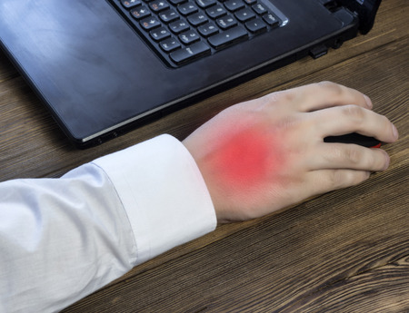 A man's hand holds a mouse while working at a computer, a pain in his hand, a close-up, a laptopの写真素材
