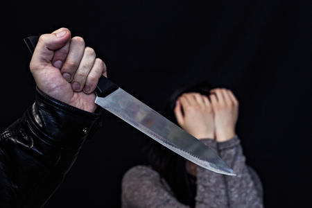 A man's hand with a knife, in the background a girl is crying, a black background, dangerの写真素材
