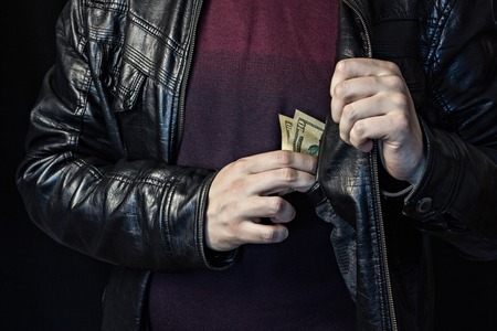 A man takes out money from a breast pocket, a black background, a black jacket, theft of money