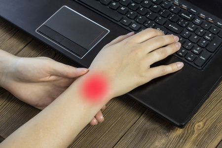 A girl holding hands behind a laptop, a painful hand, arthrosis hand, close-upの写真素材