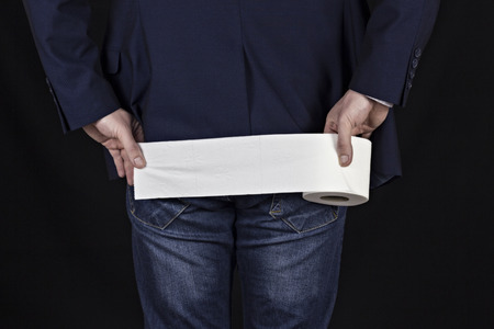 Male businessman holding a piece of toilet paper, black background, constipationの写真素材