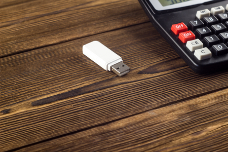 White USB flash drive and calculator on a wooden background, close-upの写真素材