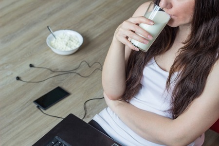 Girl drinks milk, laptop, cottage cheese, phone with headphones, close-up femaleの写真素材