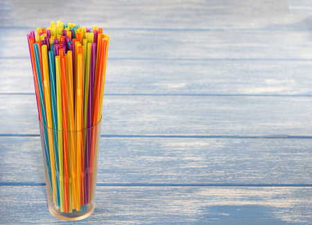 Multicolored straws for drinking in a glass, blue wooden backgroundの写真素材