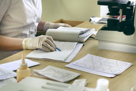 The laboratory assistant records the results of the tests in the log, the microscope and test results on the table and, glovesの写真素材