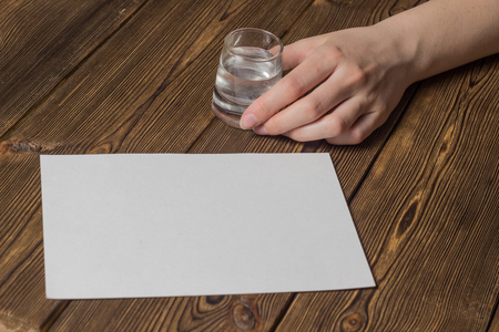 Female hand with a glass in hand and a number of clean sheet for inscriptions, wooden background, close-upの写真素材