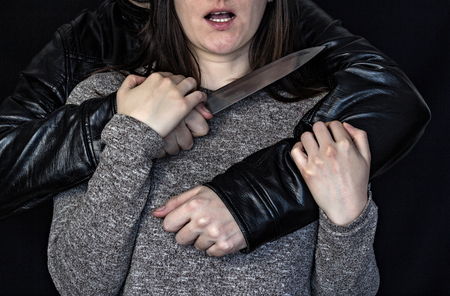Man holding a knife at the girl's throat, black background and dangerの写真素材