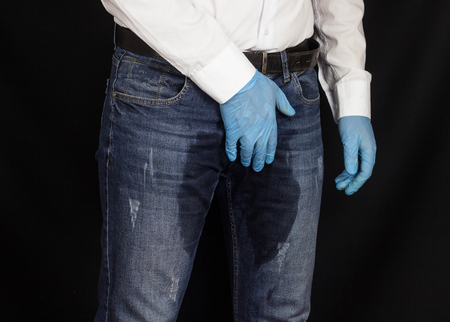 The man holds on to the perineum, the groin in the medical glove, wet pants, prostatitis, male problems, adenomaの写真素材
