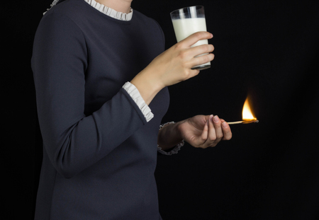 The girl on a black background holds a burning match and drinks milk, burning and pain in the stomach, heartburn and milk, gastritisの写真素材