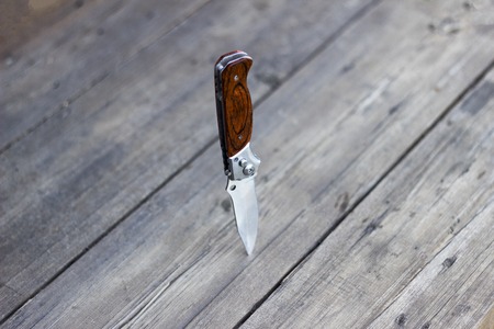 Folding knife stands in a wooden table, close-up, aggressionの写真素材