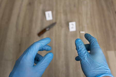 Hands of the criminalist in blue gloves against the background of evidence of a folding knife and...