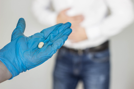 man holds on to stomach, abdominal pain, hand in glove with a pill, close-up, gastritis, stomach ulcerの写真素材