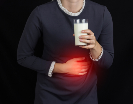 The girl holds onto her stomach and holds a glass of milk, a black background, pain and heartburn in her stomach, heartburn,の写真素材