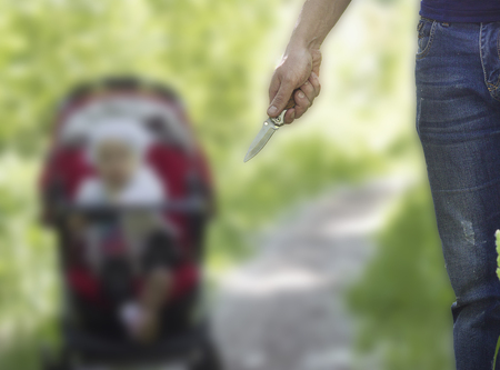 A man holds a knife in his hand against a back stroller with a child, nature, baby in a strollerの写真素材