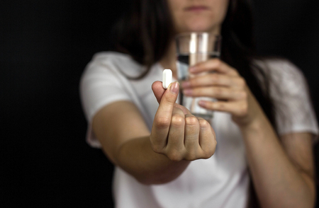Young girl holding a pill in her hand and a glass of water, close-up, black backgroundの写真素材