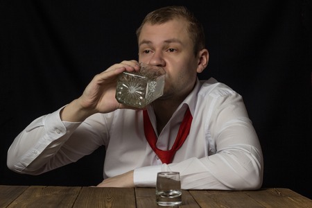 A man in a white shirt and tie drinks alcohol from a bottle, male alcoholism, black background