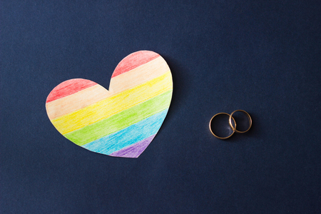Wedding rings on a blue background and a heart in the form of a flag LGBTの写真素材