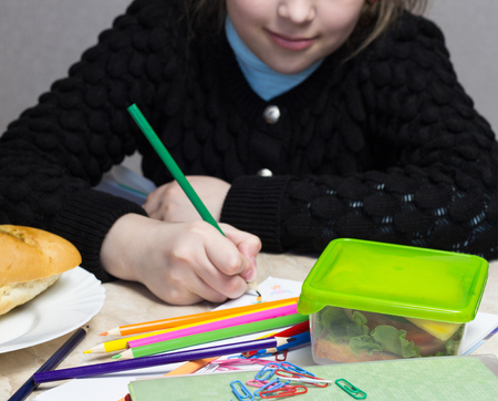 the girl does the lessons, on the table lies a sandwich, fruit, nuts, textbooks, pencilsの写真素材