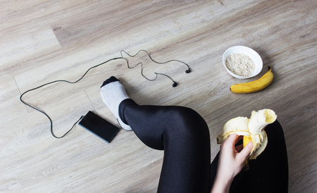 The girl eats a banana, porridge, a phone with headphones, a healthy lifestyleの写真素材