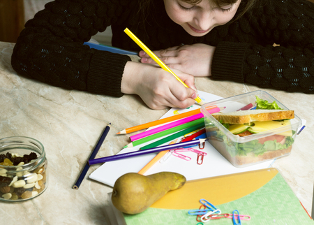 the girl does the lessons, on the table lies a sandwich, fruit, nuts, textbooks, pencilsの写真素材