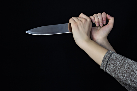 Hand of a girl with a knife on a black background, close-upの写真素材