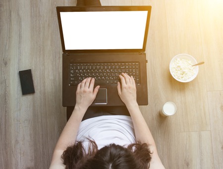 girl working behind a laptop, phone, glass of milk and a plate with cottage cheeseの写真素材