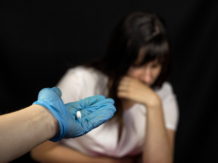 A doctor in a glove holds out to the girl a pill that feels bad, a black background, medicineの写真素材