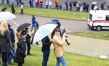 MINSK, BELARUS - JULY 3, 2018: People stand on the street with umbrellas in the rain, the girl takes off on the mobile phone an accident, an ambulanceのeditorial素材