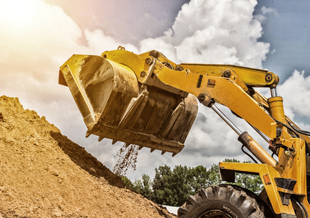 Yellow forklift lifted bucket on a pile with earth, blue skyの写真素材