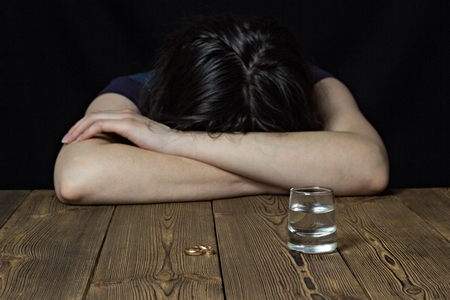 A drunk girl lies on a wooden table, laid her head on a table, a black background, female alcoholism, alcoholismの写真素材