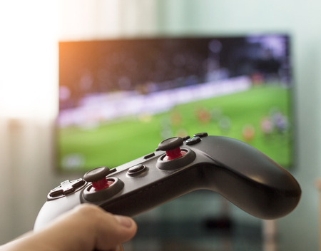 Men's hands with a joystick on the background of a TV, playing football, close-up, Champions League