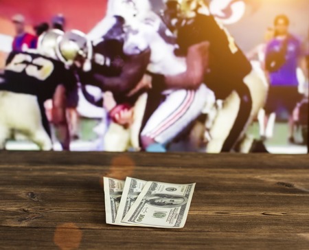 On a wooden table are money dollars on the background of a TV on which show American football, sports betting, dollars, american soccerの写真素材
