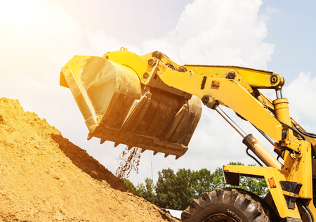 Yellow forklift lifted bucket on a pile with earth, blue skyの写真素材
