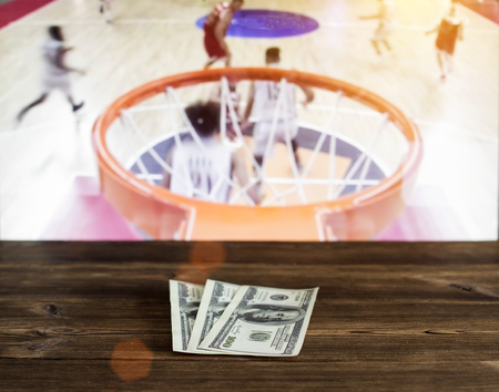 Money dollars on a wooden background on the background of a TV showing basketball, money dollarsの写真素材