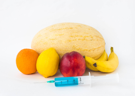 Fruits on a white background bananas, orange, melon, lemon and nectarine, next is a syringe with gmo and nitrates, nitrates, fruitの写真素材