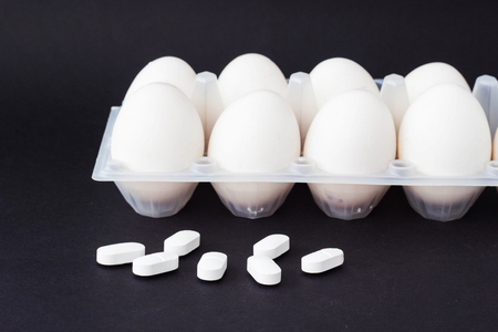 A tray of chicken eggs on a black background and next to lie pill antibiotics, close-up, pills antibiotics and testiclesの写真素材