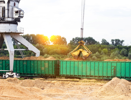 Port cargo crane loads wood chips into railway cars, material, sunsetの写真素材