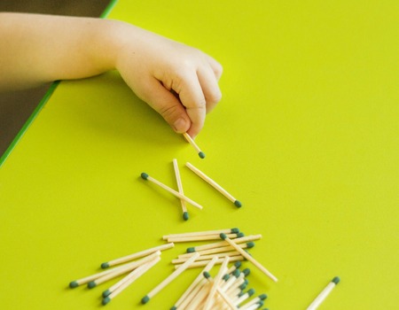 A small child holds a match in the hand on a green background, close-up, danger, fire, child and...