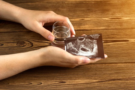 Female hand holds a glass with alcohol and a shot of uzi pregnancy, alcohol and pregnancy, a wooden background, gestation alcoholの写真素材