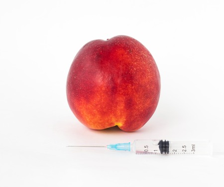 Nectarine on a white background, next is a syringe with gmo and nitrates, close-up, geneticaly, toxinの写真素材