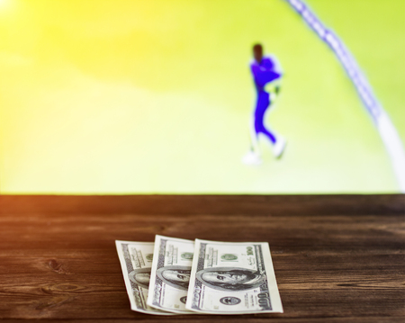 Money dollars on the background of a TV on which there is a sport game of cricket, sports betting, dollarsの写真素材