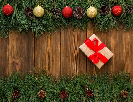 Box with a gift tied with a red ribbon for the holiday to the new year and Christmas, wooden background with fir branches and Christmas ballsの写真素材