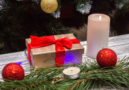 New Year's gift and a burning candle with Christmas balls toys on a white wooden background, New Year's holidays, a gift for the new yearの写真素材