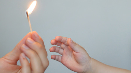 the hand of an adult man holds a burning match, the hand of a child reaches for a burning match, close-up, fire, copy-space, dangerous, lucifer matchの写真素材
