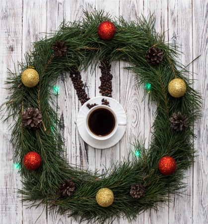 Christmas clock made of fir branches, clock hands of pine nuts, a cup of coffee and Christmas toys on a white wooden background, holidayの写真素材
