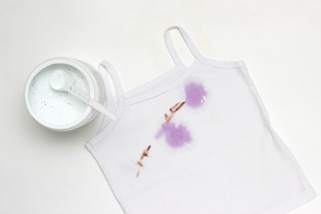 Children's white T-shirt with spots, next to the container with stain remover, close-up, white background, whitenerの写真素材