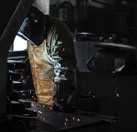 Welder at the factory welds metal parts, welding and sparks, dirty production, harmfulness, fireの写真素材
