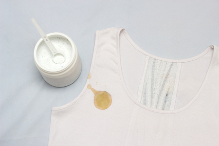A spot on a white T-shirt, next to it is a container with a stain remover, close-up, whitenerの写真素材