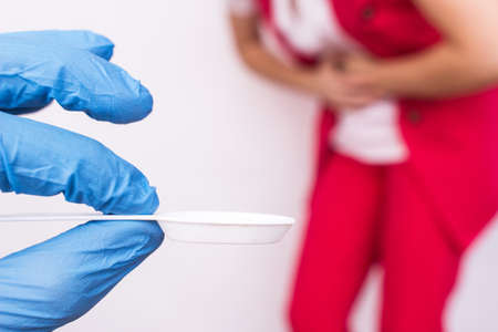 Doctor in a medical glove holding a spoon with medicine in the background a girl holding her stomach, stomach pain, gastritis, close-up, Helicobacterの写真素材