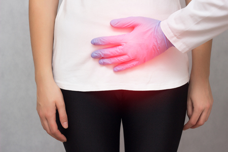A doctor in medical gloves holds a girl by the lower abdomen which has problems with menstruation and pain, hyperthyroidism, close-up, gynecology, diseaseの写真素材